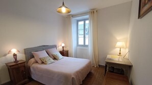 Un dormitori amb un llit, dues taules de nit amb làmpades, una finestra amb cortines i un terra de fusta.