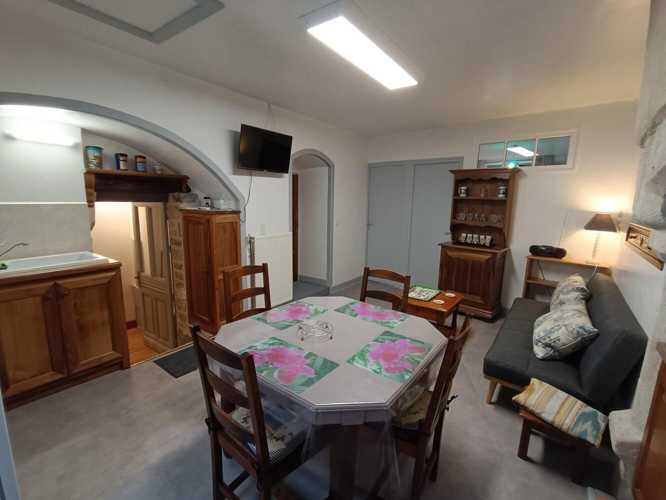 Un espace de vie compact comprenant une table à manger, des chaises, un canapé, un téléviseur et un coin cuisine avec des placards et un plan de travail.