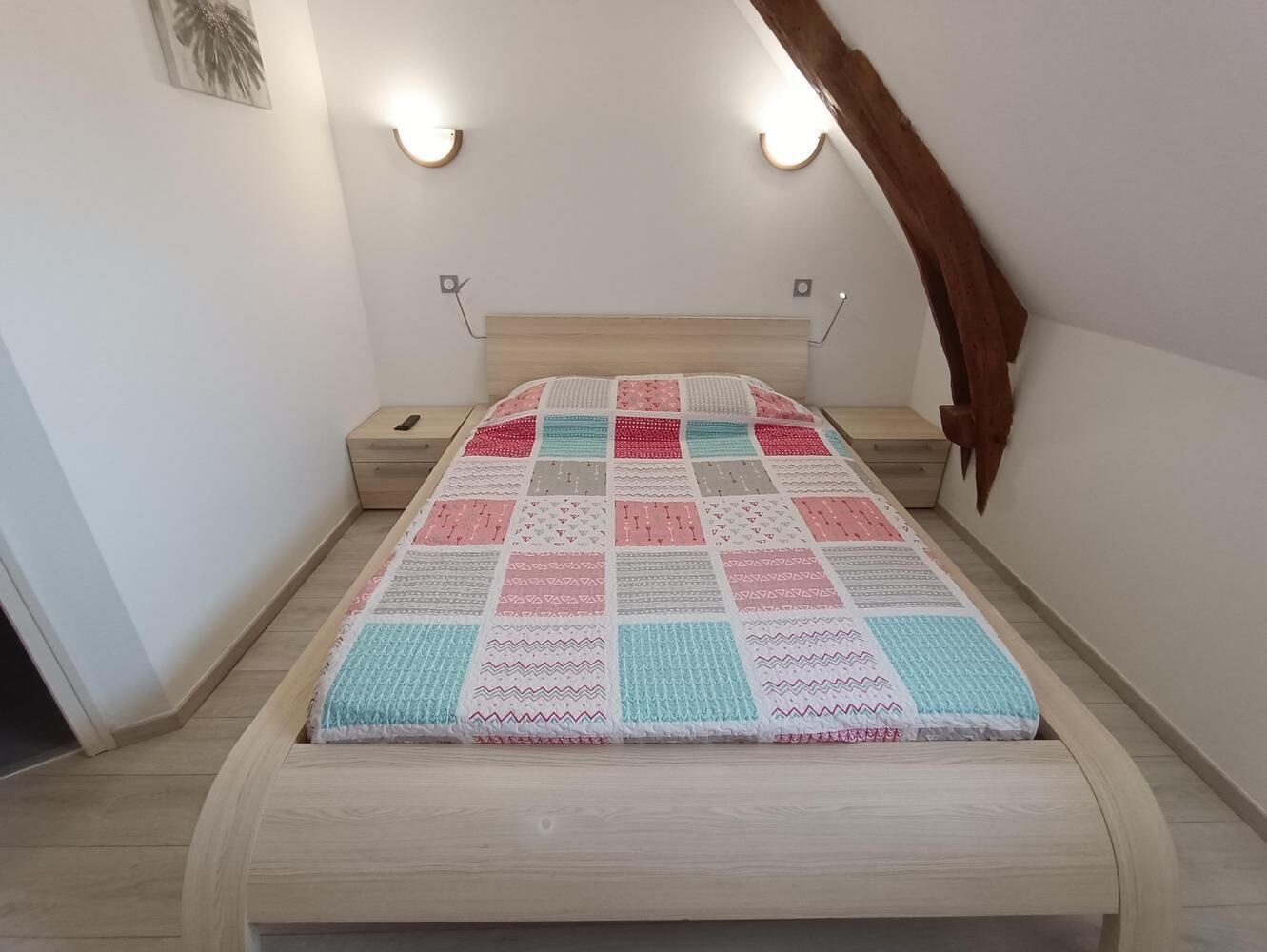 A bedroom with a wooden bed, a quilt, and two wall-mounted nightstands.