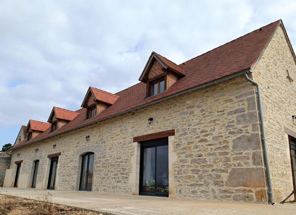 Un bâtiment en pierre avec un toit recouvert de tuiles rouges, de nombreuses fenêtres et une grande porte vitrée.