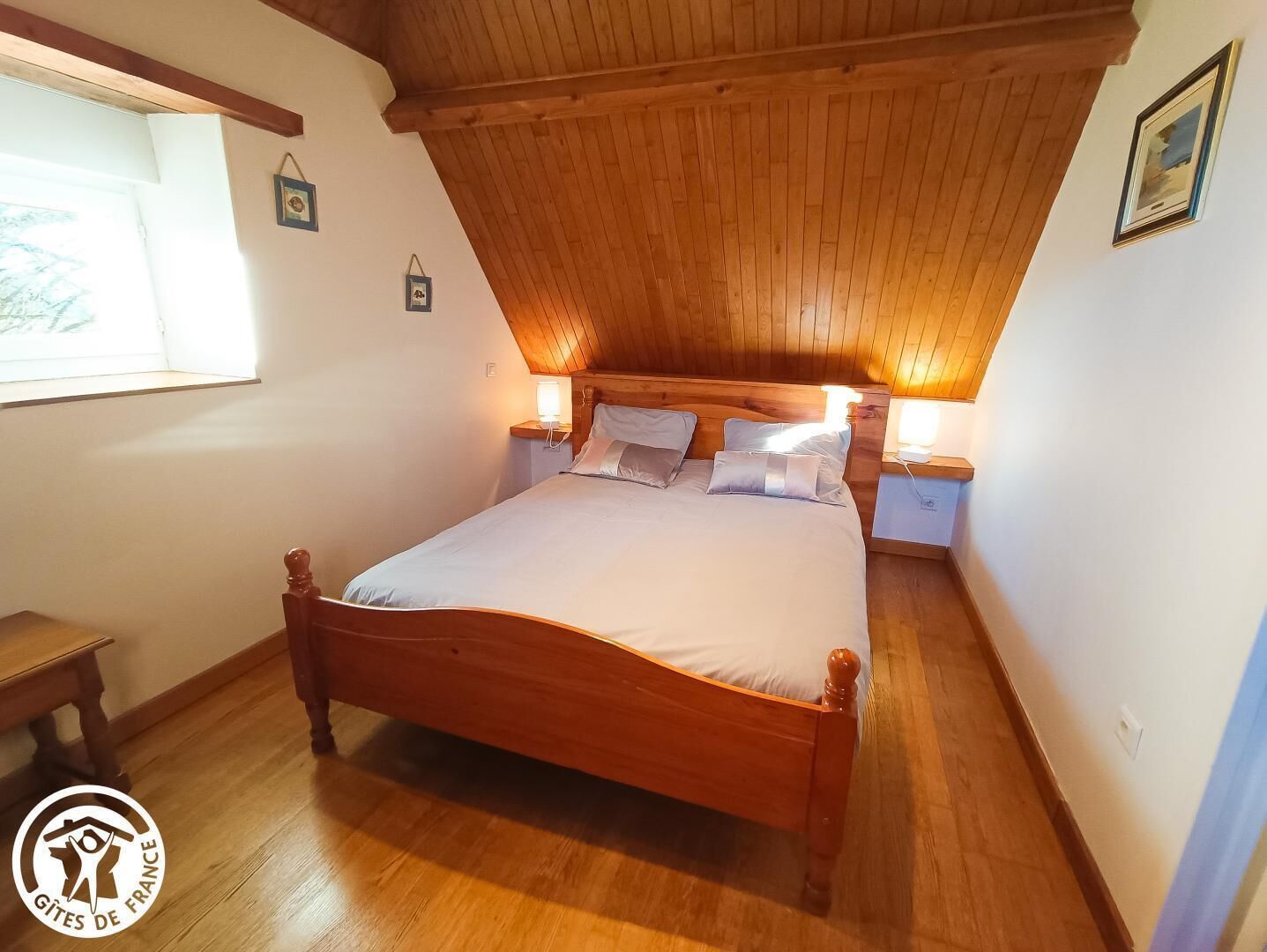 Une chambre avec un plafond en bois, un grand lit, des lampes de chevet et une fenêtre.