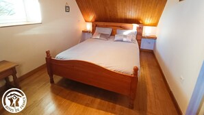 Quarto com teto de madeira, uma cama grande, luminárias de cabeceira e uma janela.