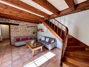 A cozy living area with a stone wall, two sofas, a wooden table, and a wooden staircase.