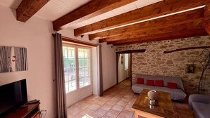 Uma sala de estar com televisão, parede de pedra, teto de madeira e sofá.
