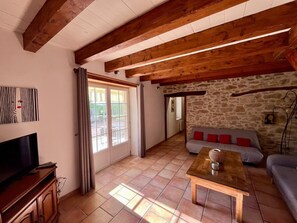 Una sala de estar con televisión, pared de piedra, techo de madera y un sofá.