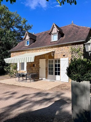 A stone house with a covered patio, a door, and a window. - Gîtes de France® - La Grangette (LISSAC ET MOURET)