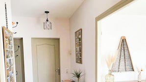 A hallway with a wooden floor, a door, a small table with a plant, and a wooden cabinet with shelves. - Gîtes de France® - Chez Septi (FIGEAC)