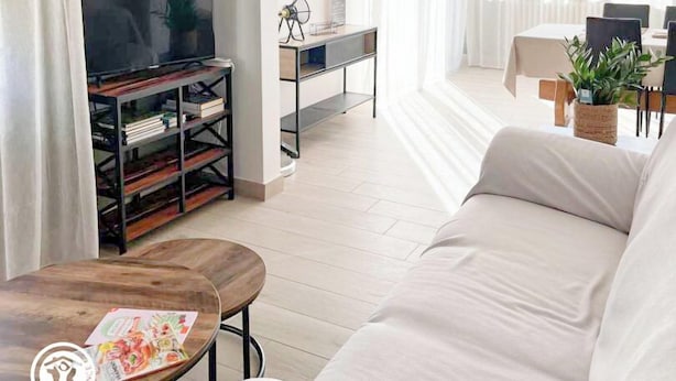 A modern living room with a sofa, a coffee table, a TV on a stand, a dining area with a table and chairs, and a kitchen area with a sink and cabinets. - Gîtes de France® - Chez Septi (FIGEAC)