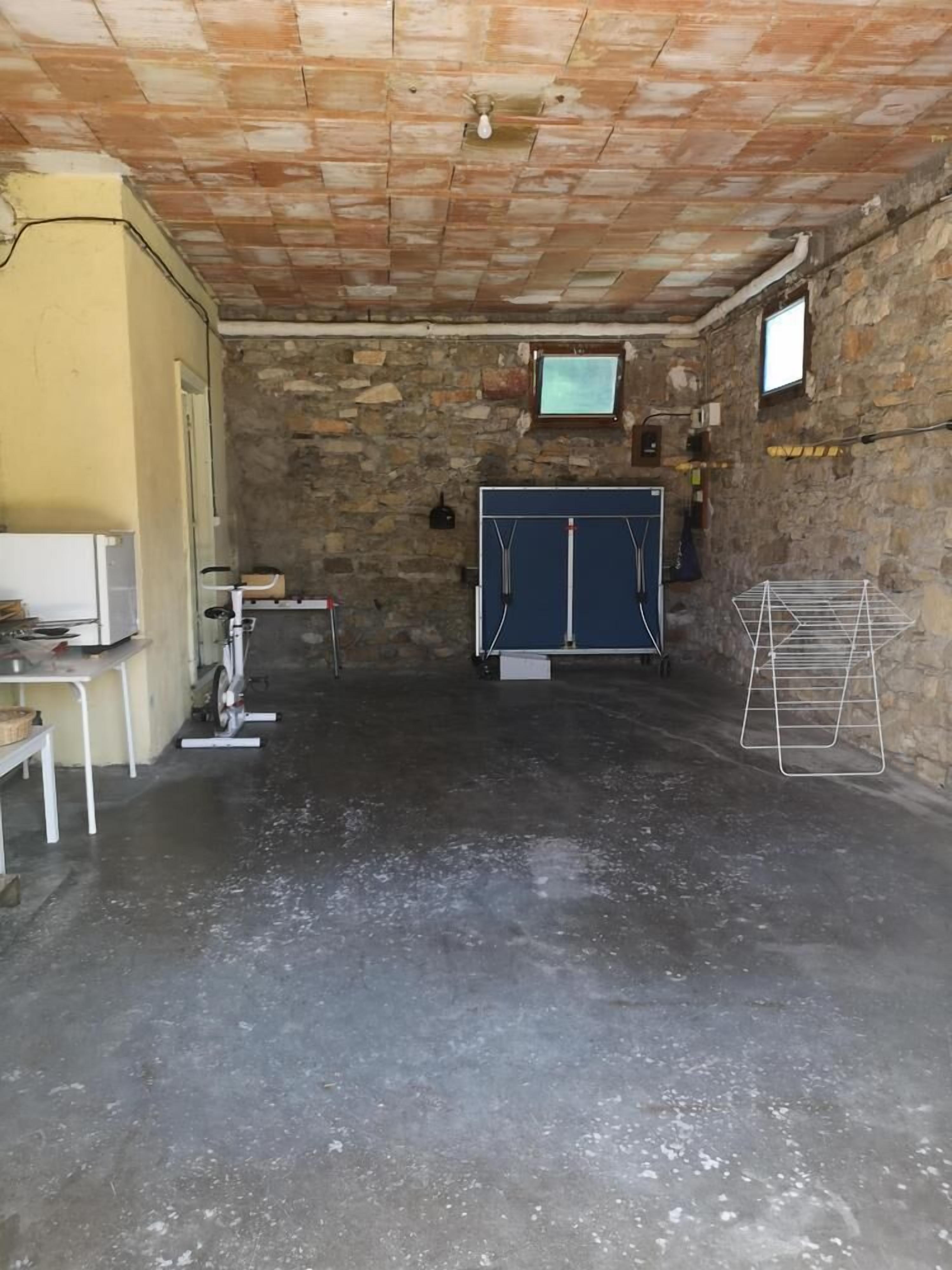 Une pièce avec une table de ping-pong, un coin pour faire la lessive et un mur en pierre.