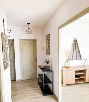 A hallway with a wooden floor, a door, a small table with a plant, and a wooden cabinet with shelves.