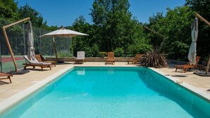A rectangular swimming pool with clear blue water, surrounded by wooden lounge chairs and umbrellas. - Gîtes de France® - Manon (CASSAGNES)