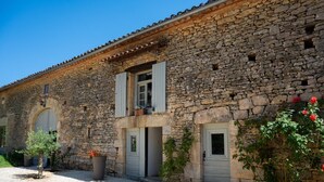 A stone building with two windows and a door, surrounded by gravel and plants. - Gîtes de France® - Manon (CASSAGNES)