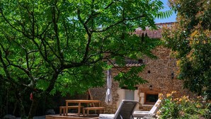 A stone building with a tiled roof, surrounded by lush greenery and a gravel patio. - Gîtes de France® - Manon (CASSAGNES)