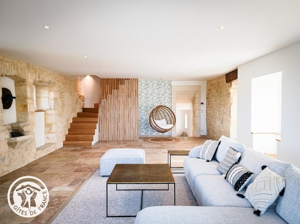 Ein modernes Wohnzimmer mit Steinwand, einer Holztreppe, einem Hängesessel und einem Sofa mit gemusterten Kissen.