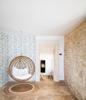 A room with a stone wall, a hanging chair, and a patterned wallpaper.