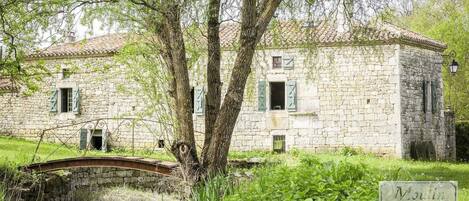 A stone building with a rustic charm, a small bridge, and lush greenery.