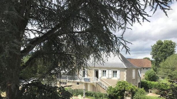 A two-story house with a balcony, surrounded by a well-maintained garden with various plants and a paved pathway. - Gîtes de France® - "Chez Destraux" The Restaurant (TAURIAC)