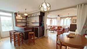 A modern kitchen with a central island, dining area with a round table and chairs, and a living room with a sofa and chairs. - Gîtes de France® - "Chez Destraux" The Restaurant (TAURIAC)