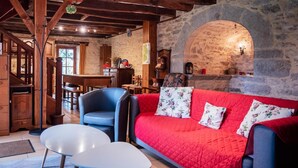 A cozy room with a stone wall, a red sofa with floral cushions, a blue armchair, and a white table.