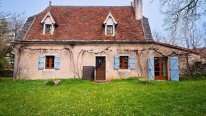 A stone house with a steeply pitched roof, a central door, and two windows with shutters.