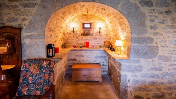 A stone-walled room with a bench, a wooden cabinet, and a patterned chair.