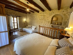 A rustic bedroom with a large bed, a smaller sofa, a wooden chair, and a stone wall. - Gîtes de France® - The Dovecote at Peyralat   (SAINT-CERNIN PECHS DU VERS)
