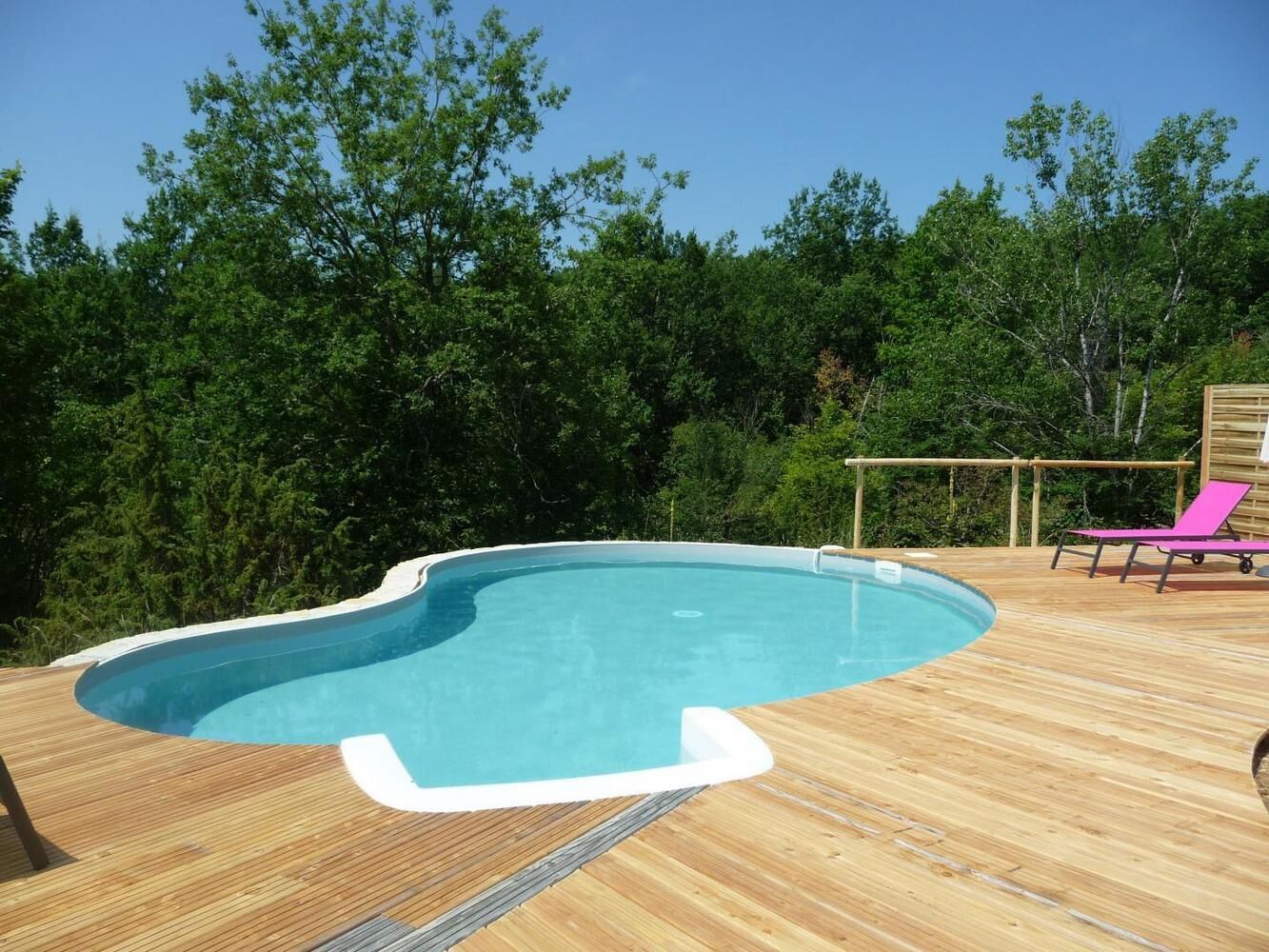 Une terrasse en bois avec une piscine, entourée d’arbres.