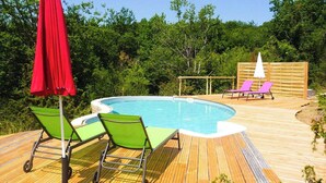 A wooden deck with a swimming pool, green and pink lounge chairs, and a red umbrella. - Gîtes de France® - La Bouyssounade (CRAYSSAC)