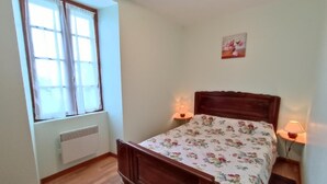 Quarto com cama de madeira, duas luminárias de cabeceira, um radiador e uma janela com cortinas.