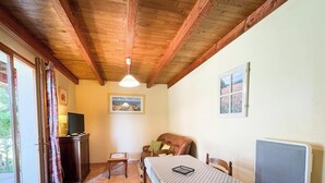 Een kamer met een houten plafond, een bed met hoofdeinde, een tafel, een stoel, een televisie op een kast en een raam met gordijnen.