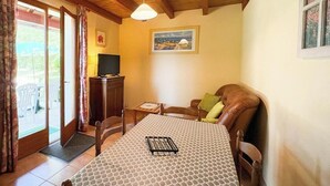 Een gezellige kamer met een houten plafond, een eettafel met een tafelkleed met patroon, een televisie op een kast en een schilderij aan de muur.