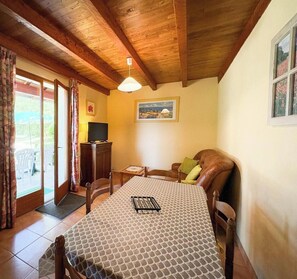 A cozy room with a wooden ceiling, a dining table with a patterned tablecloth, a television on a cabinet, and a painting on the wall. - Gîtes de France® - La Martio (SOUSCEYRAC EN QUERCY)