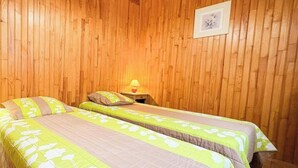 Een kamer met twee bedden, houten wanden, een lijst met foto en een nachtkastje met lamp.
