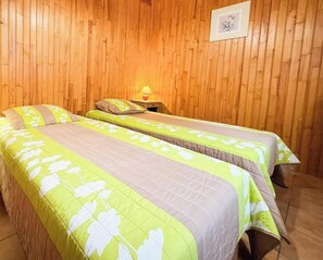 Et værelse med to senge, trævægge, et billede i ramme og et natbord med en lampe.