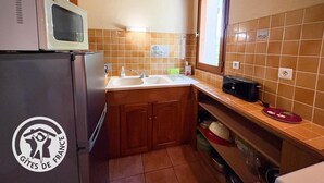 Een keuken met houten kastjes, een koelkast, een magnetron, een spoelbak en een raam.