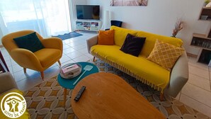 A living room with a yellow sofa, a yellow armchair, a TV, and a painting on the wall.