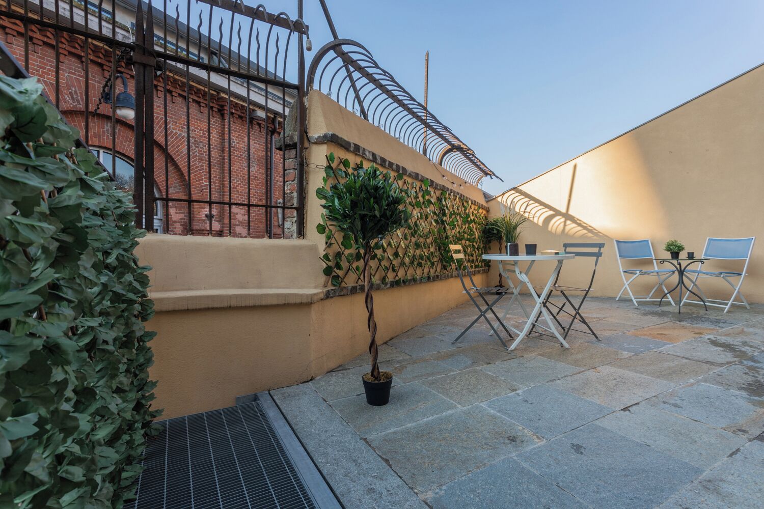 A patio with a table and chairs, a potted plant, and a metal fence.