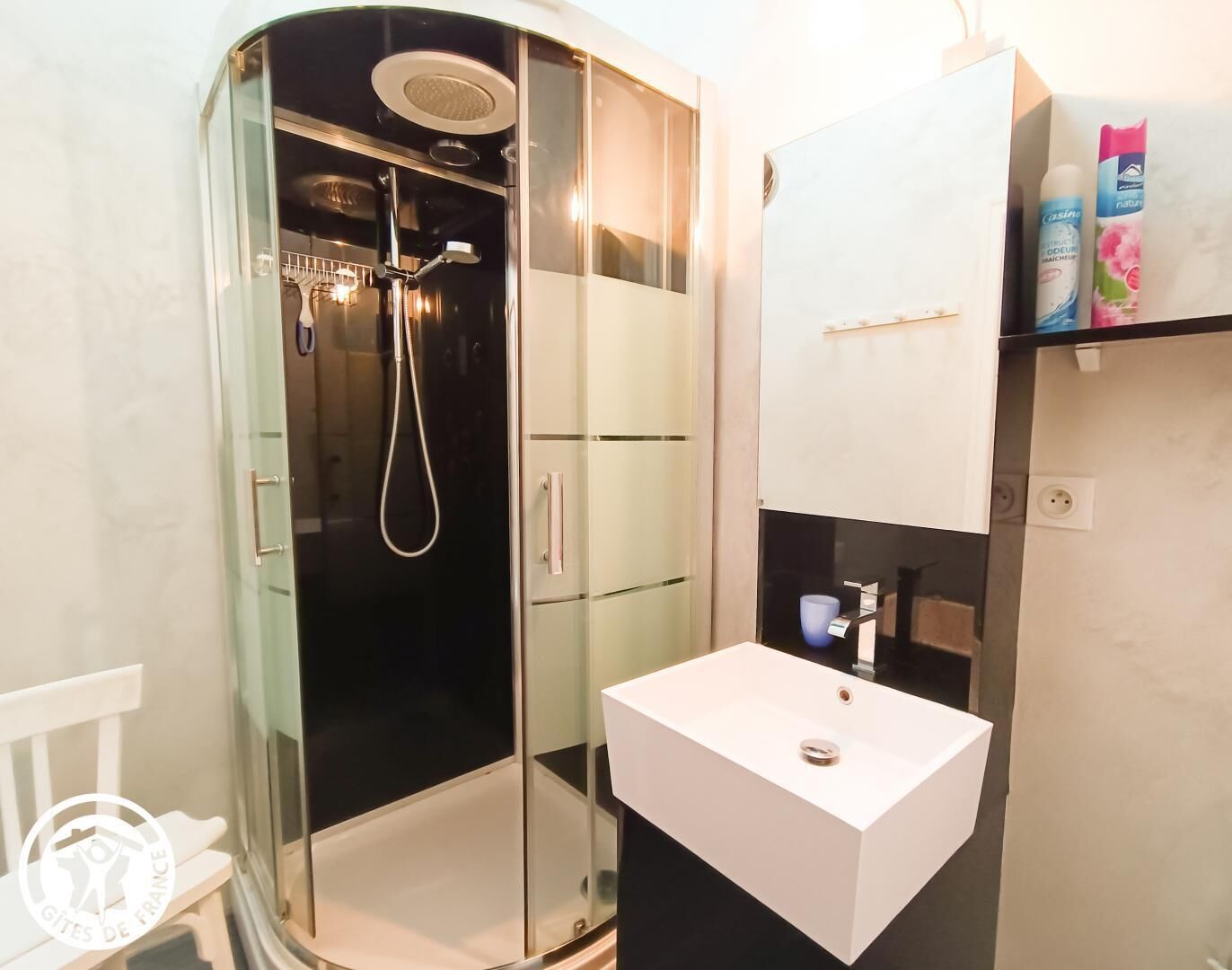 Un baño moderno con ducha acristalada, lavamanos blanco y mueble de tocador con artículos de aseo.