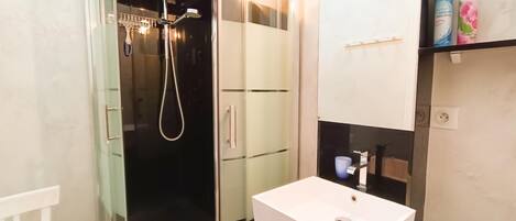 Un baño moderno con ducha acristalada, lavamanos blanco y mueble de tocador con artículos de aseo.
