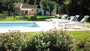 Ein Swimmingpool mit Liegestühlen, umgeben von einem gepflegten Garten und einem Haus im Hintergrund.