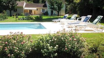 A swimming pool with lounge chairs, surrounded by a well-maintained garden and a house in the background.