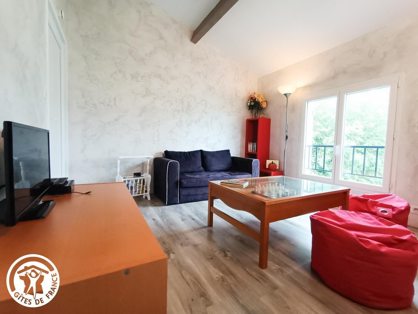 A room with a wooden desk, a sofa, a glass-top coffee table, and a red bean bag.