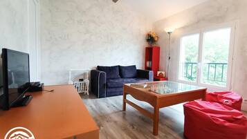 A room with a wooden desk, a sofa, a glass-top coffee table, and a red bean bag.