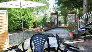 Un patio con mesa y sillas, rodeado de macetas y un muro de piedra.