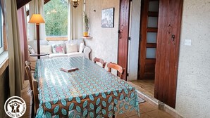 Un comedor acogedor con una mesa cubierta por un mantel estampado, un sofá con cojines, una lámpara colgante y una puerta de madera.