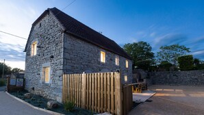 A stone building with a sloped roof, a wooden fence, and a paved driveway. - Gîte Ventoulou - Thegra (THEGRA)