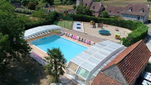 A swimming pool with a glass enclosure, surrounded by lounge chairs and a small play area. - Gîte Ventoulou - Thegra (THEGRA)