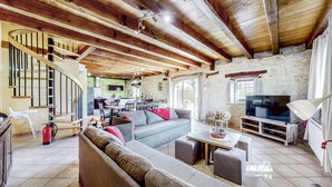 A spacious living area with a wooden staircase, a dining area, and a TV. - Gîte Ventoulou - Thegra (THEGRA)