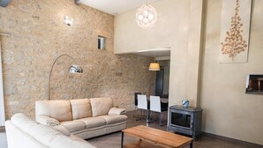 A modern living room with a stone wall, a beige sofa, a wooden coffee table, and a dining area with chairs and a table. - Gîtes de France® - 46G12322 (SAUZET)