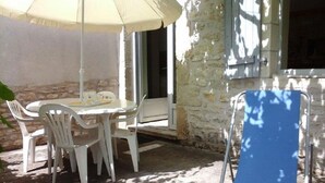 An outdoor seating area with a table and chairs, a blue folding chair, and a white umbrella. - Gîtes de France® - LA TOUR (CREYSSE)